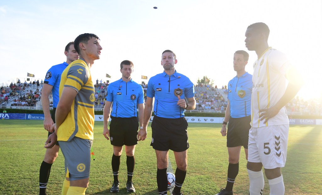 Captains Danny Griffin of the Riverhounds and Leland Archer of the Charleston Battery watch as referee Thomas Snyder flips the coin before the teams' match June 8, 2024, at Patriots Point Soccer Complex in Mount Pleasant, S.C. (Photo courtesy of the Charleston Battery)